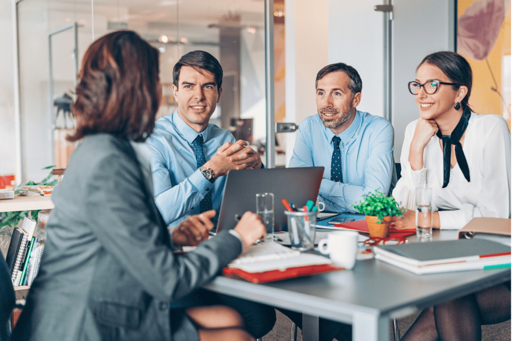 Team di lavoro seduto attorno a un tavolo, con computer portatili e documenti sparsi, mentre discutono e collaborano su un progetto in un ambiente d'ufficio moderno.