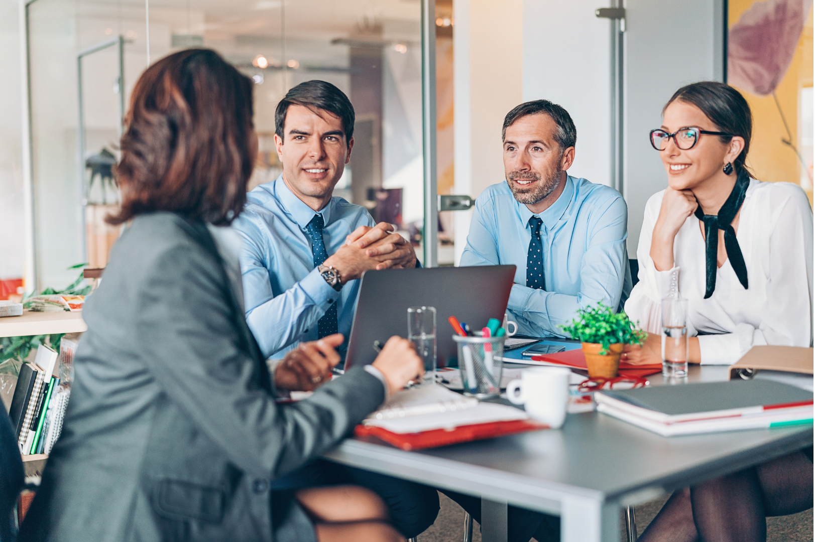 Team di lavoro seduto attorno a un tavolo, con computer portatili e documenti sparsi, mentre discutono e collaborano su un progetto in un ambiente d'ufficio moderno.