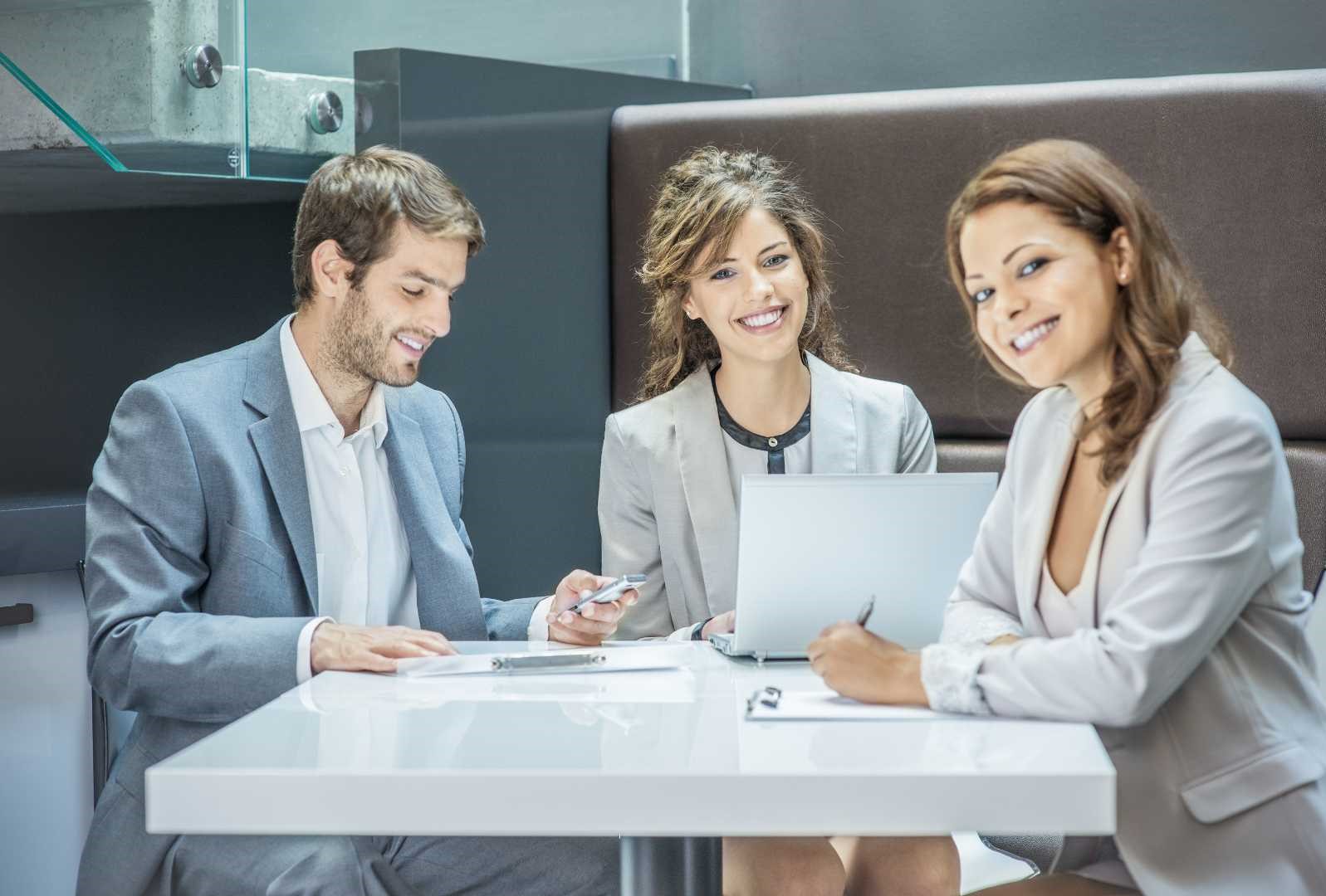 Consulenti del lavoro seduti a una scrivania, circondati da computer portatili e documenti, mentre discutono e analizzano pratiche professionali in un ambiente d'ufficio moderno e organizzato.