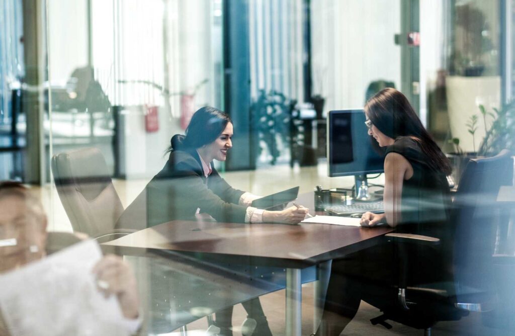 Consulenti seduti a una scrivania, con computer portatile e tablet davanti a loro, mentre discutono e analizzano dati, in un ambiente di lavoro professionale e tecnologicamente avanzato.