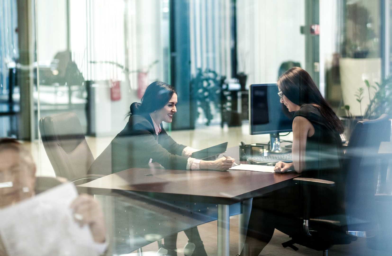 Consulenti seduti a una scrivania, con computer portatile e tablet davanti a loro, mentre discutono e analizzano dati, in un ambiente di lavoro professionale e tecnologicamente avanzato.