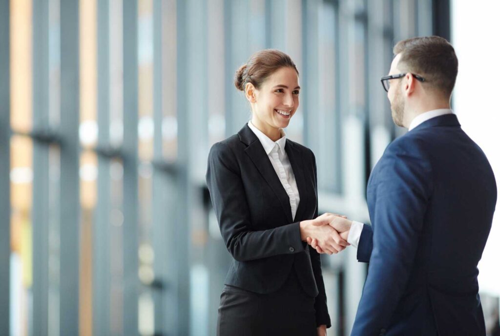 "Consulenti in abbigliamento professionale, discutono sul luogo di lavoro mentre si stringono la mano, in segno di accordo o collaborazione, in un ambiente aziendale.