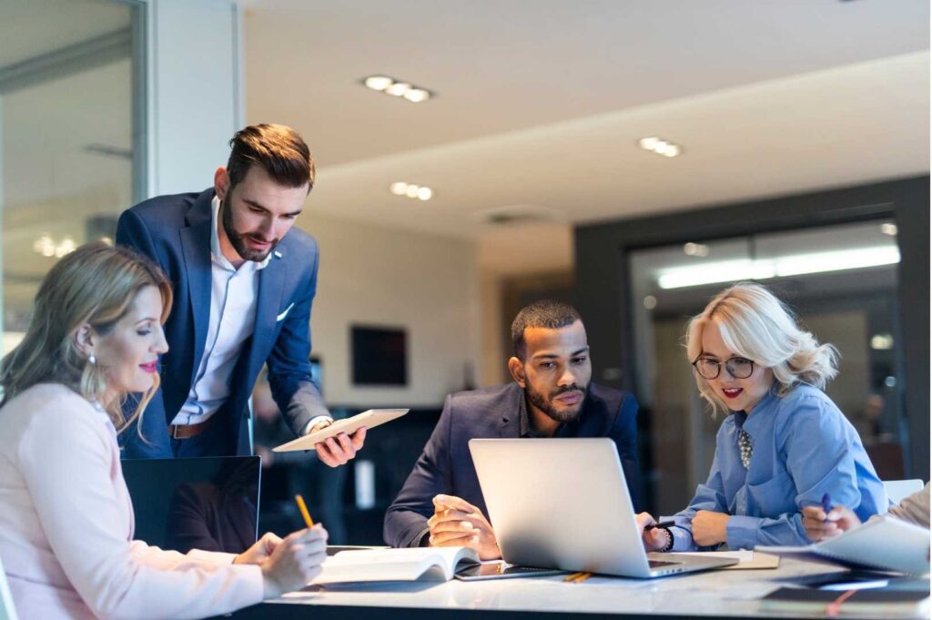 Consulenti specializzati nella digitalizzazione fiscale, seduti attorno a un tavolo, discutono tra loro mentre consultano appunti e lavorano su computer, collaborando su soluzioni tecnologiche per il settore fiscale.