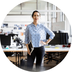 Donna dipendente di Leyton in piedi, vestita in abbigliamento professionale, tiene un iPad tra le mani, con un'espressione concentrata, pronta per una presentazione o una consulenza.