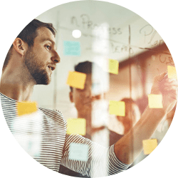 Team di Leyton, composto da donne e uomini in abbigliamento professionale, consulta dei post-it colorati su una parete o su un tavolo, discutendo idee e strategie in un ambiente di ufficio moderno.