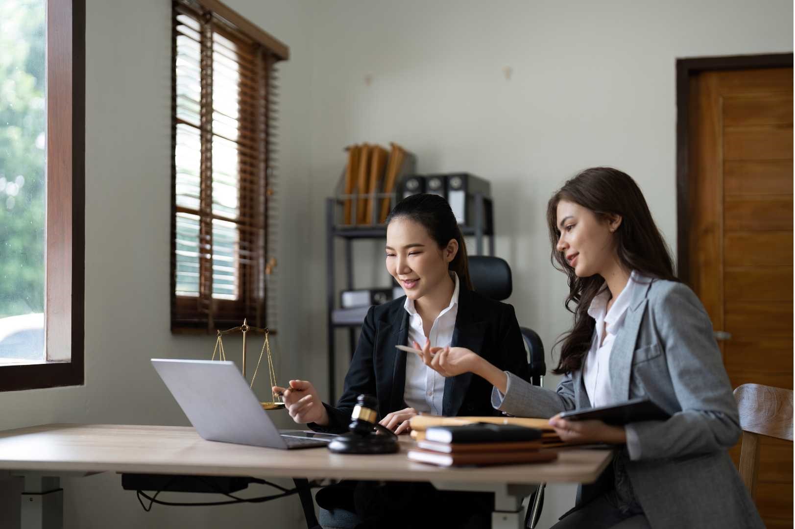 Due avvocate che lavorano insieme in un ufficio moderno, consultando documenti legali e un laptop. Collaborazione professionale e assistenza legale esperta.