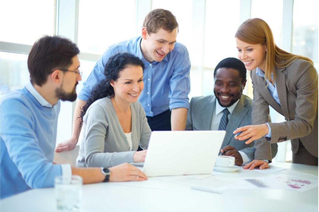 Team di lavoro composto da persone che collaborano con computer portatili, discutendo e scambiando idee in un ambiente professionale, simbolo di cooperazione digitale e produttività.