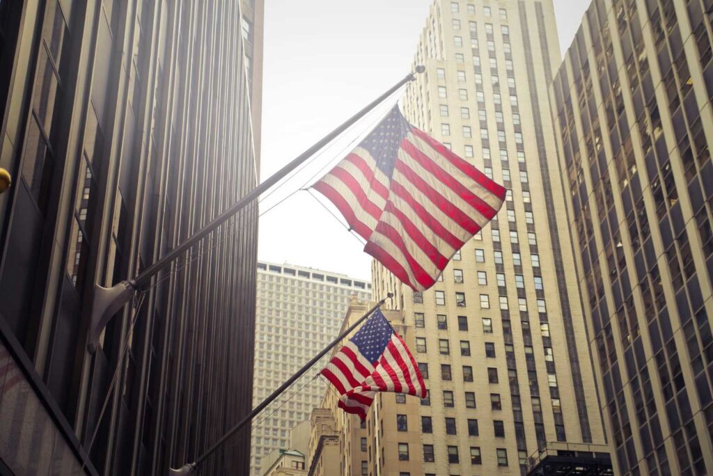 Bandiera americana sventola orgogliosamente tra i grattacieli di New York City, simbolo di libertà e unità. Trump e commercio estero.