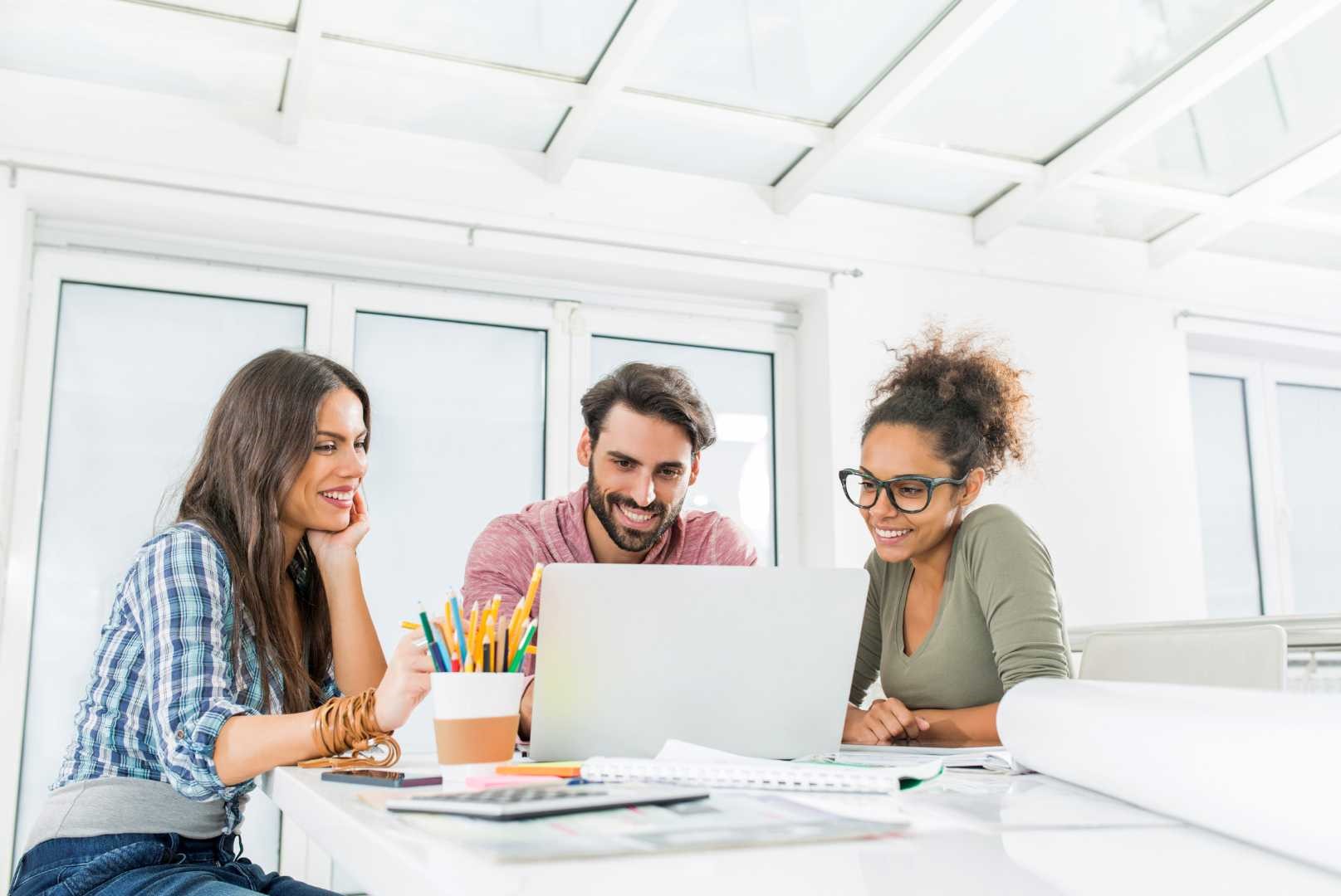 Team di lavoro che utilizza computer portatili per collaborare, con un ambiente aziendale sullo sfondo, simbolo di lavoro remoto e cooperazione digitale in un contesto professionale.