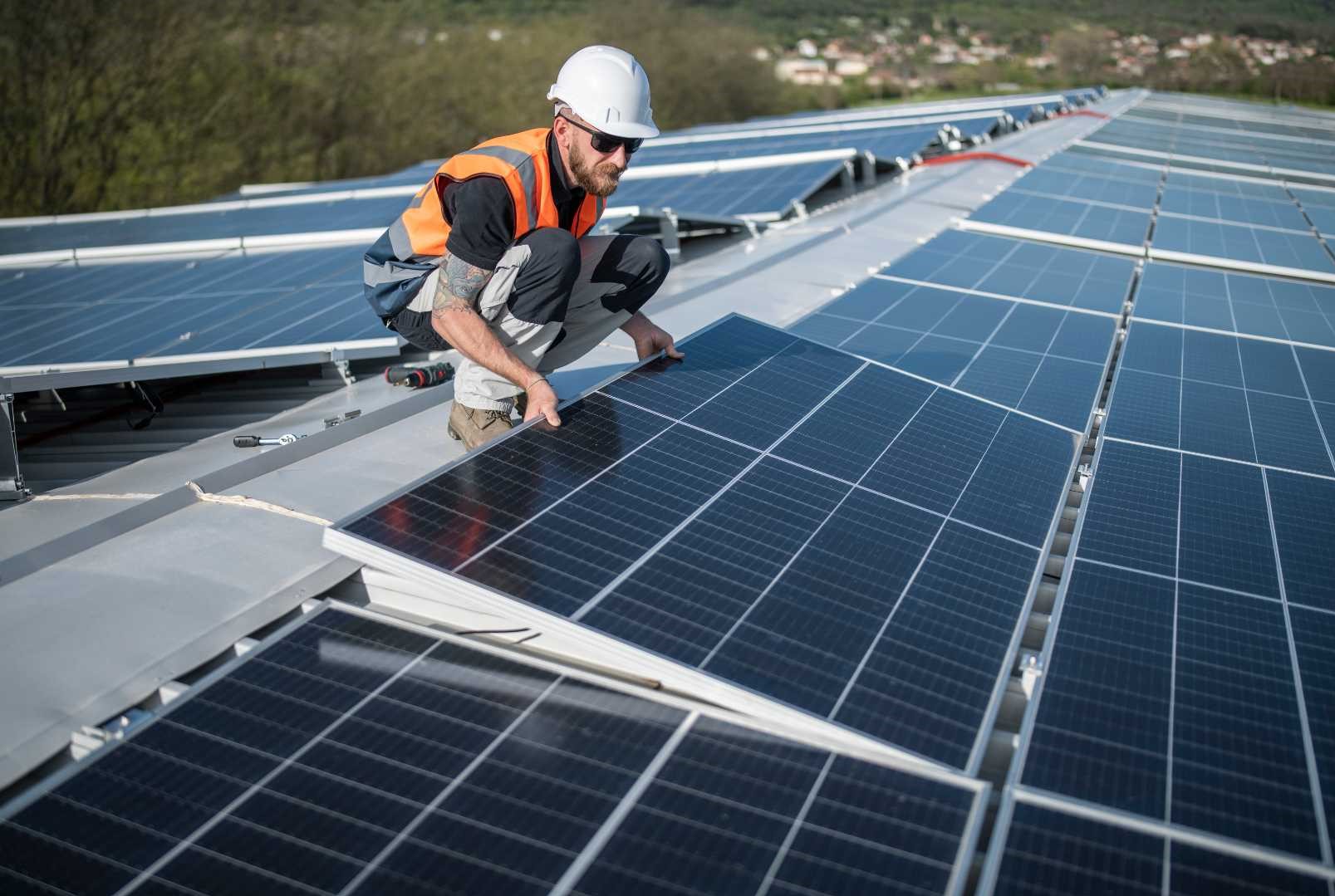 Un uomo installa un pannello solare su un tetto, mentre il sole splende nel cielo azzurro.