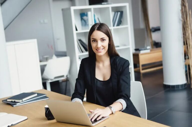 Una donna sorride mentre lavora con il suo computer portatile.