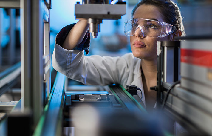 Una donna con degli occhiali prottetivi lavora con un macchinario industriale.