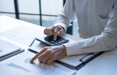 Business professional calculating capital allowances and reviewing financial investment documents with charts and graphs in a modern office setting