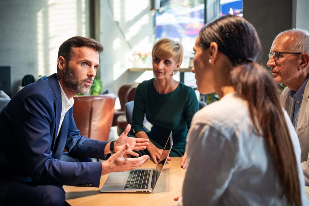 Team meeting around a laptop in a modern office, with one person speaking and others listening.