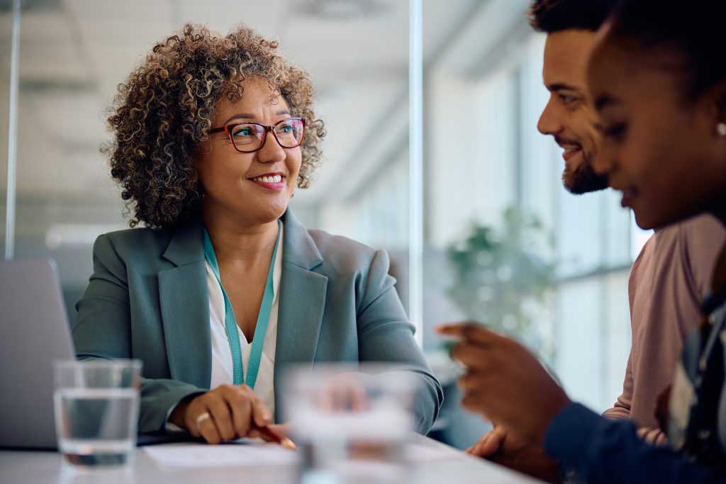 Happy real estate agent and young couple going through paperwork during a meeting in the office.